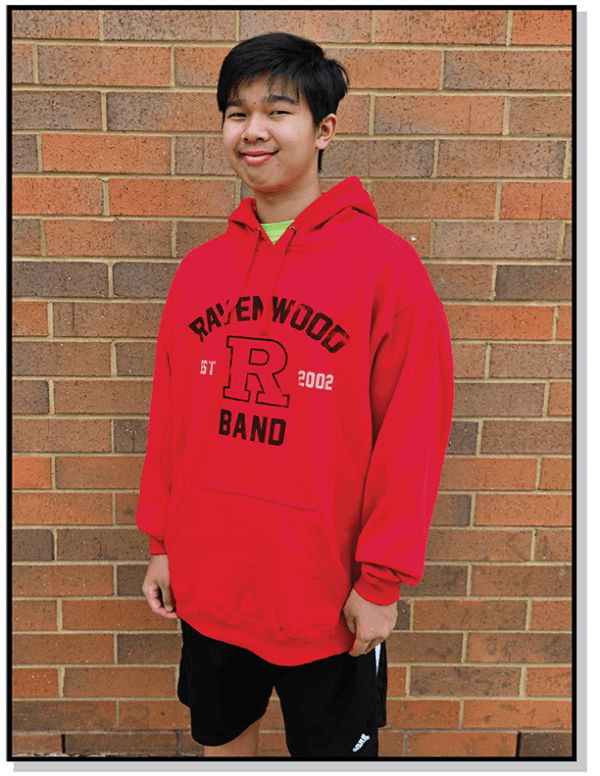 A boy in red hoodie standing next to brick wall.